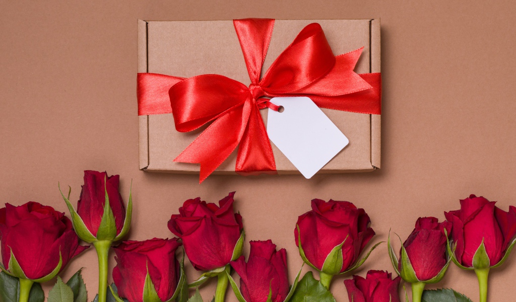 Подарок с красным бантом на бежевом фоне с красными розами
