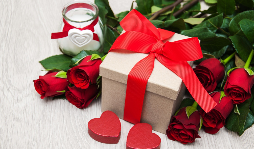Красивый букет красных роз на столе со свечой и подарком