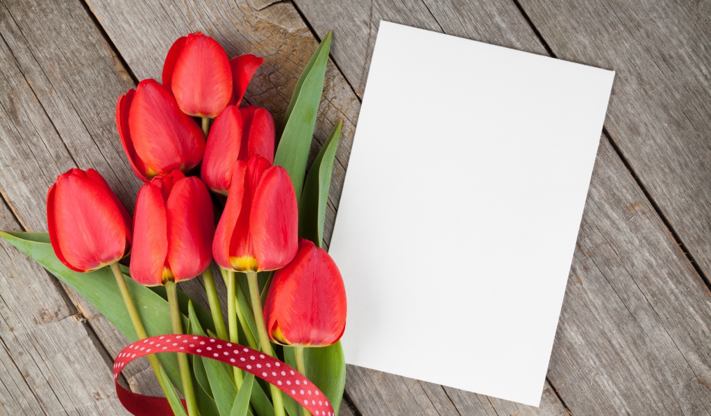 Букет красных тюльпанов с листом бумаги на деревянном столе