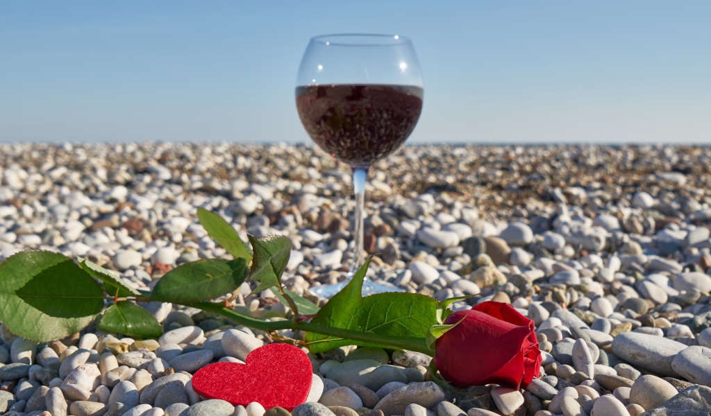 Красная роза на морской гальке с сердечком и бокалом вина