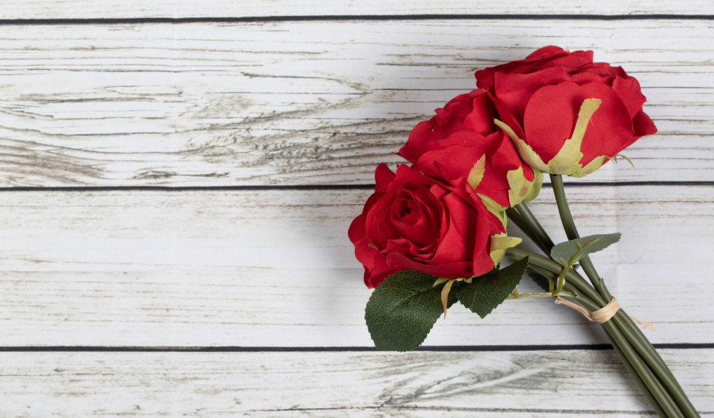 Три искусственные красные розы на деревянном фоне