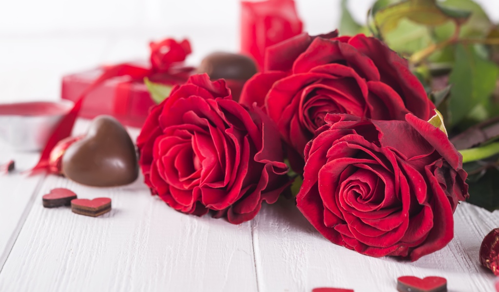 Три красивые красные розы на столе с конфетами