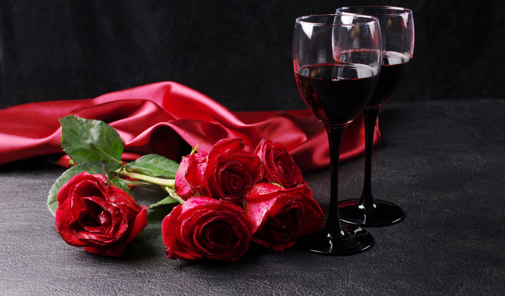 Два бокала с красным вином на черном фоне с букетом красных роз