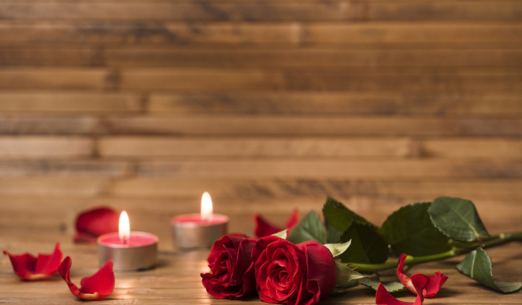 Две красные розы на столе с зажженными свечами 