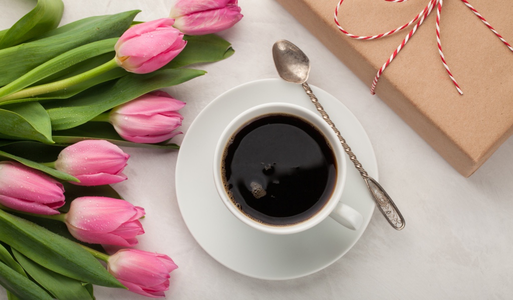 Белая чашка кофе на столе букетом розовых тюльпанов и подарком