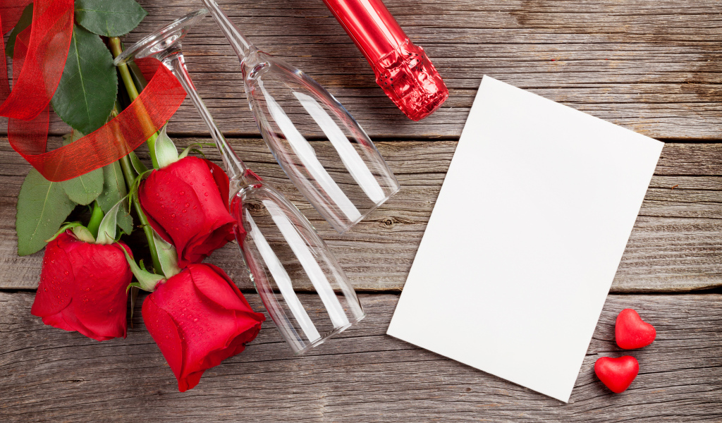 Белый лист бумаги на деревянном столе с бокалами и красными розами