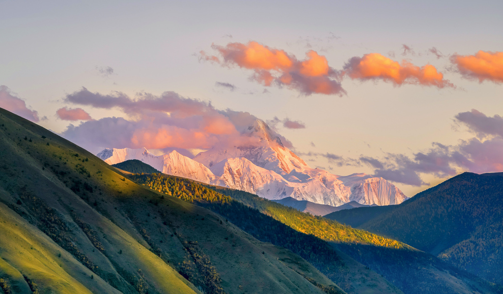 Заснеженные вершины гор у зеленых холмов под голубым небом