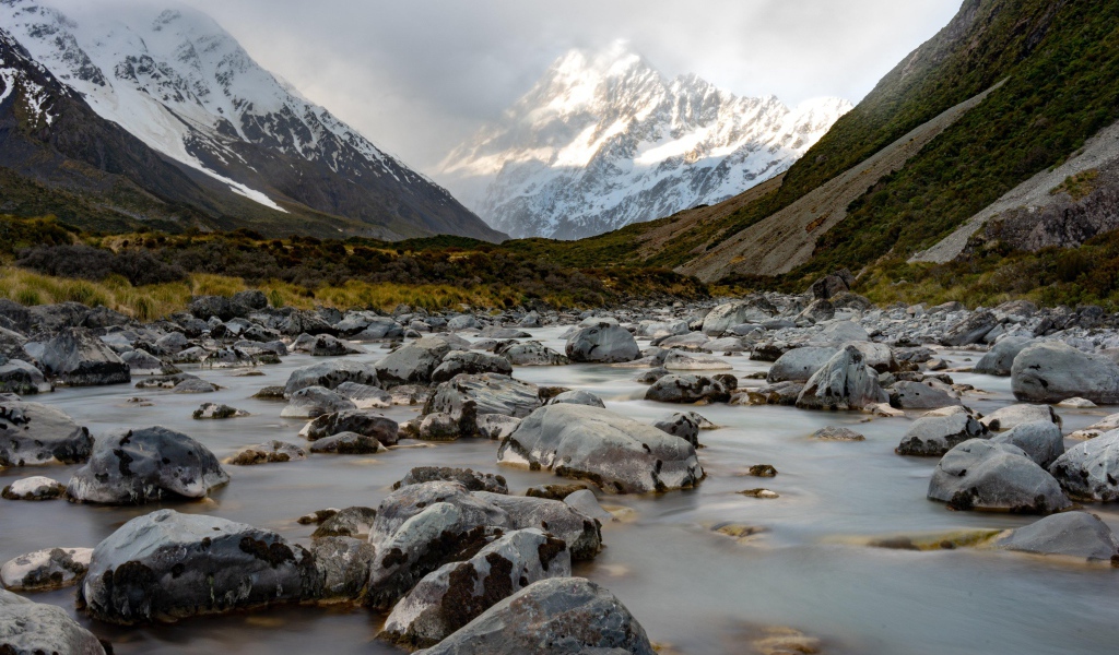 Камни в воде у заснеженных гор 