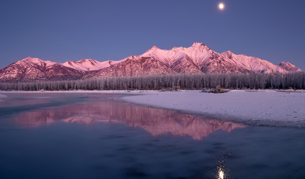 Луна над заснеженными горами отражается в заледеневшем озере 