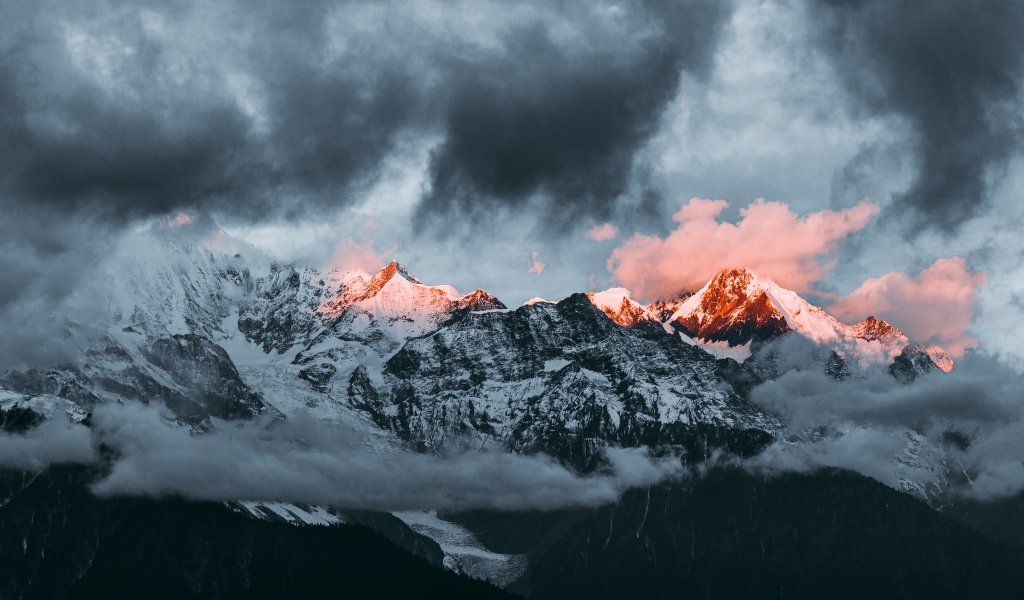 Солнце на рассвете освещает вершины заснеженных гор 