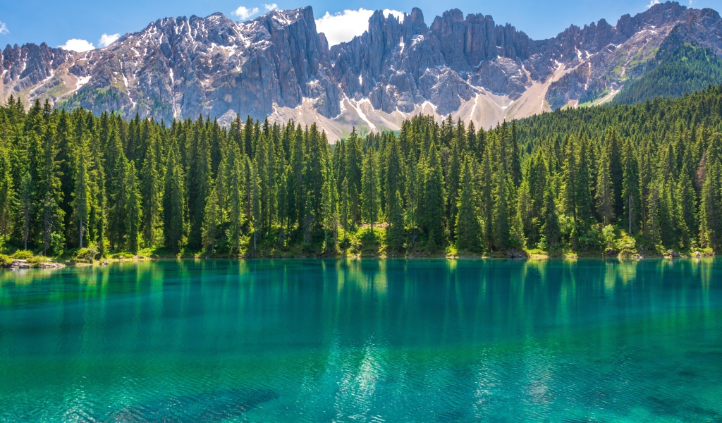 Красивое озеро с голубой водой у хвойного леса на фоне гор