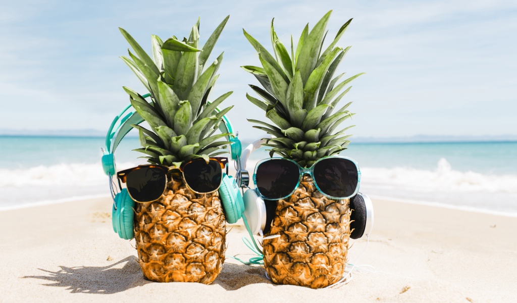 Два ананаса на пляже в солнечных очках и наушниках