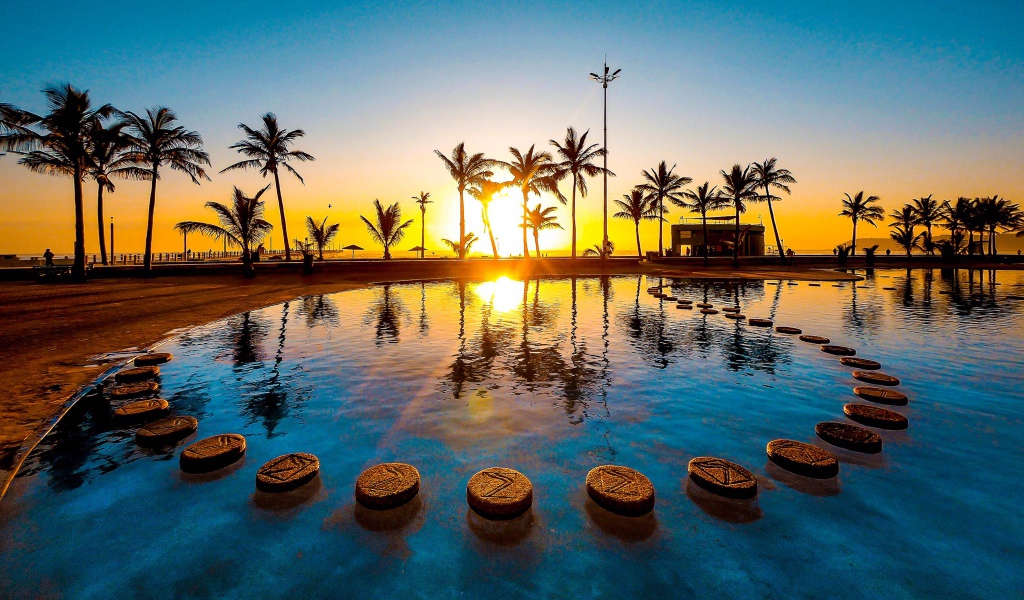 Закат солнца на тропическом пляже на фоне бассейна