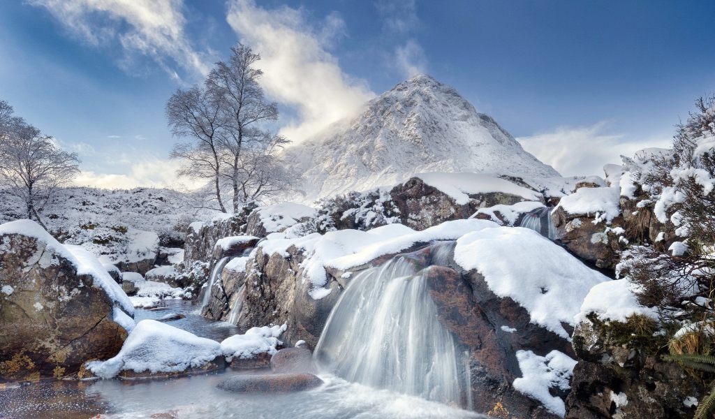 Водопад стекает с камней на фоне заснеженной горы