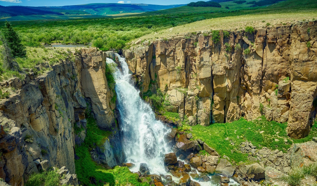 Быстрая вода водопада стекает по утесу на фоне голубого неба