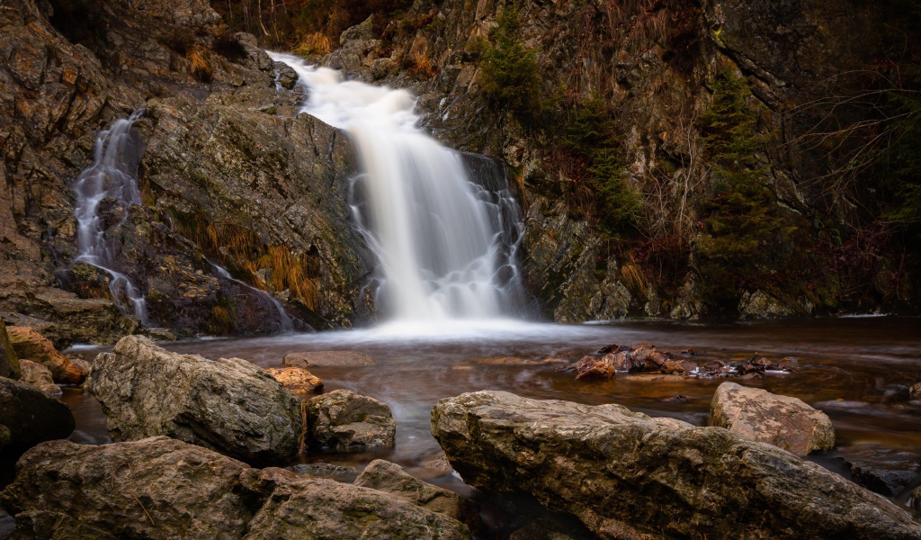 Быстрая вода водопада стекает по камням в горную реку