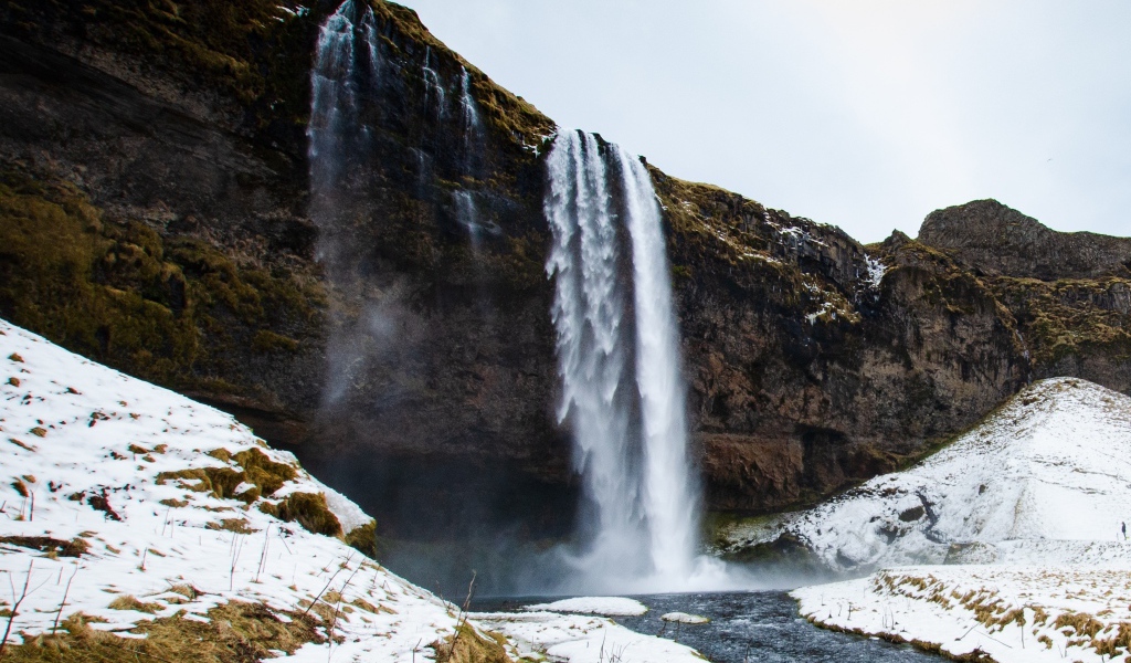 Водопад стекает со скалы в реку с покрытыми снегом берегами