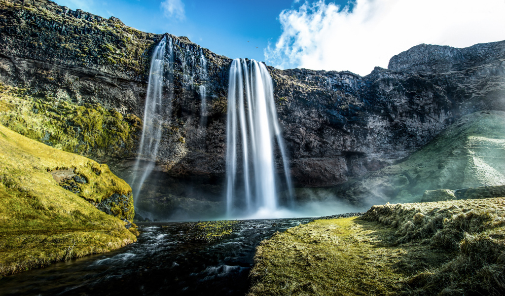 Водопад стекает с гор на фоне голубого неба