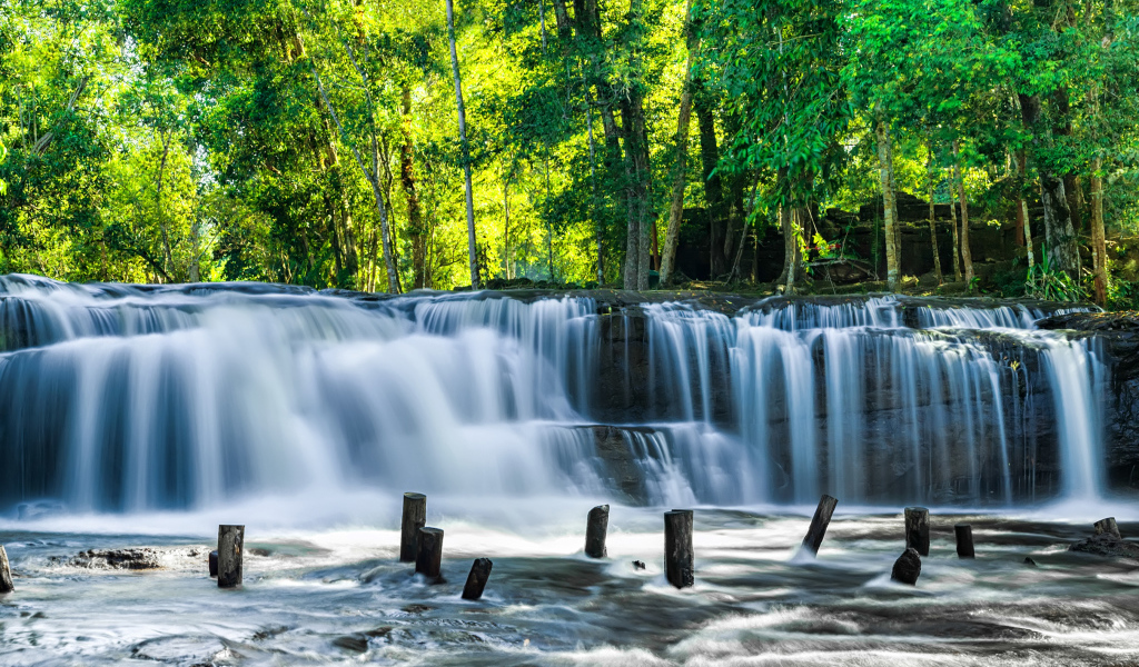 Водопад стекает с камней у зеленых деревьев
