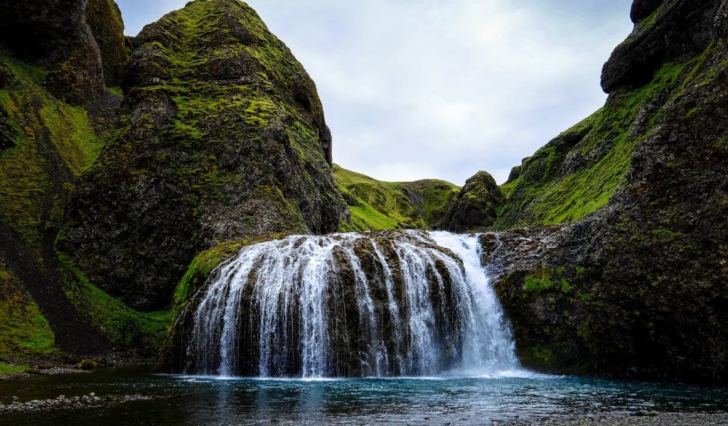 Белая вода водопада стекает по покрытым мхом скалам