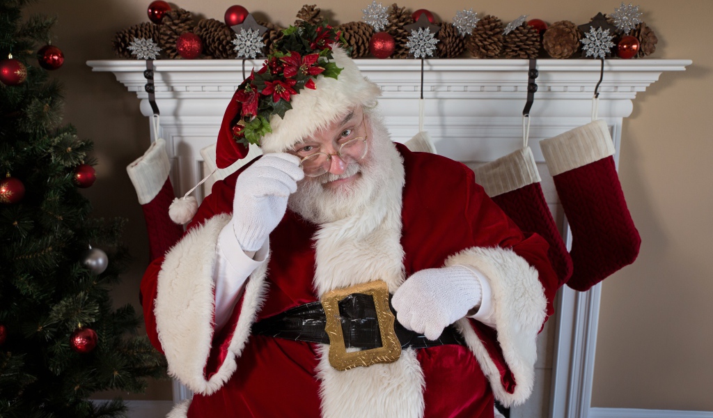 Санта Клаус в очках сидит у камина у новогодней елки