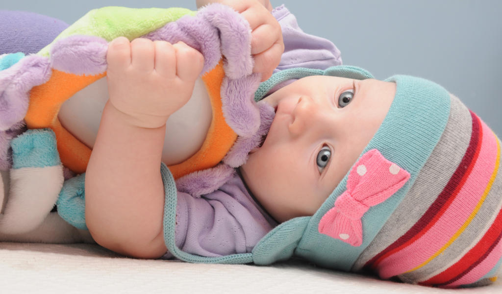 Младенец в шапке грызет мягкую игрушку