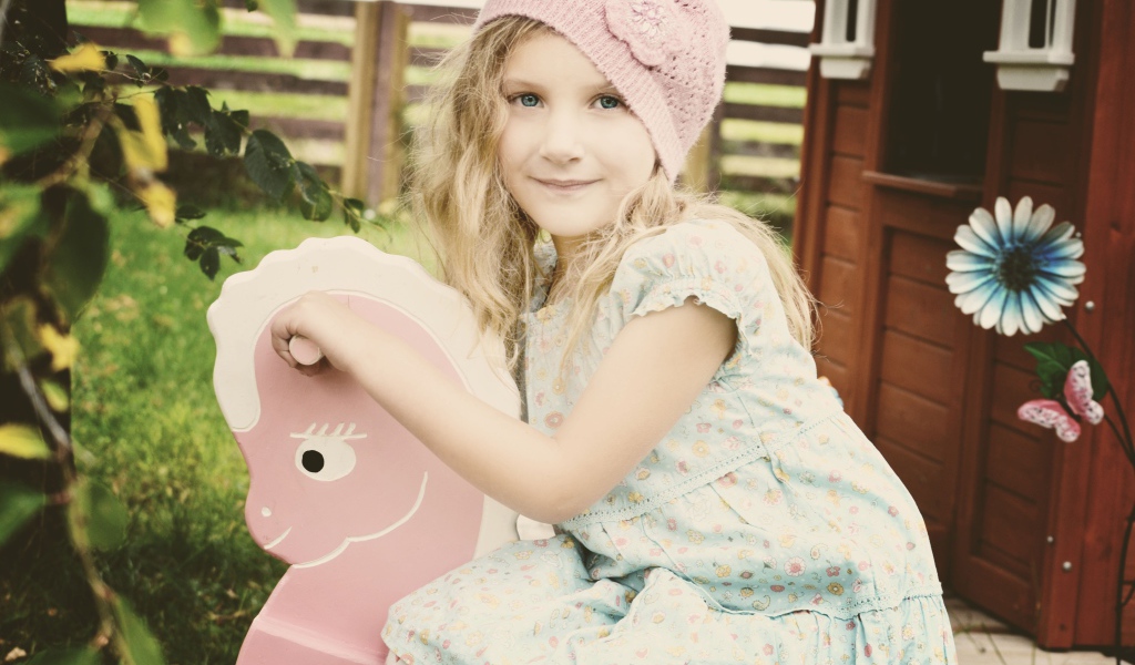 Девочка в платье сидит на деревянной лошади