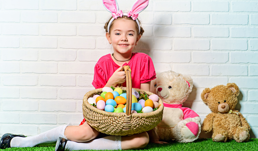 Улыбающаяся девочка сидит у стены с корзиной пасхальных яиц и игрушками