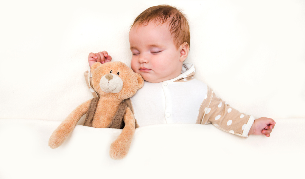 Грудной ребенок спит с плюшевым мишкой на белом фоне