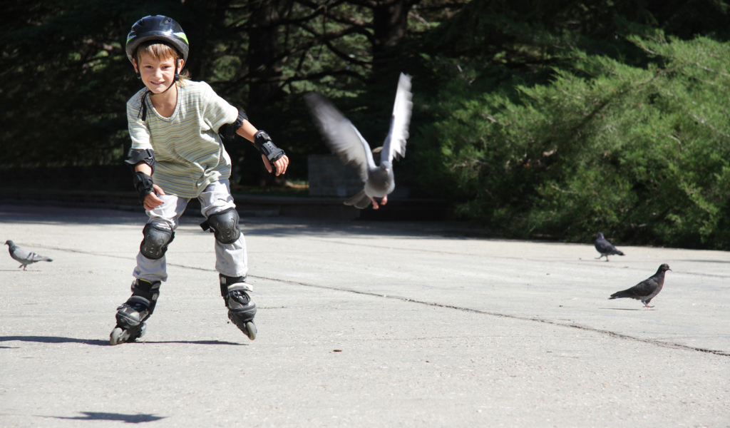 Мальчик катается на роликах на асфальте с голубями