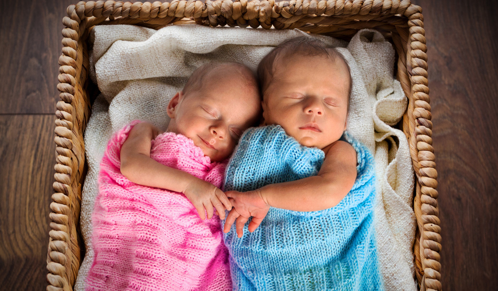 Грудные мальчик и девочка спят в плетеной корзине