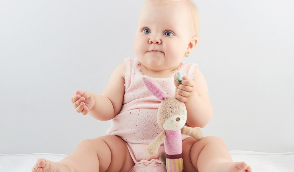 Смешной малыш с игрушкой сидит на сером фоне