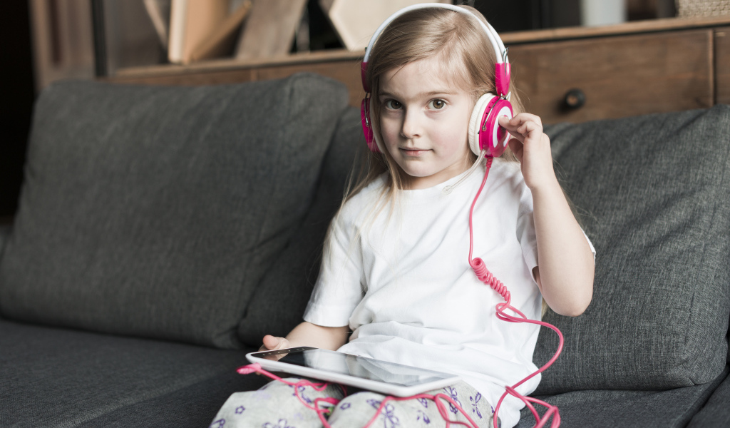 Девочка сидит на диване в наушниках  и с планшетом
