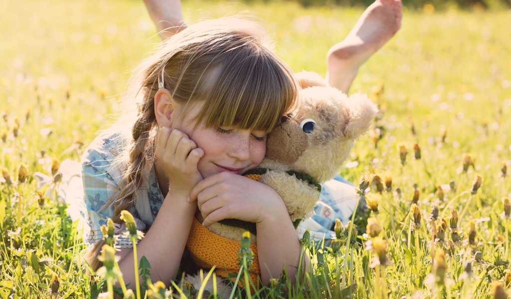 Девочка с игрушкой в руках лежит на траве 