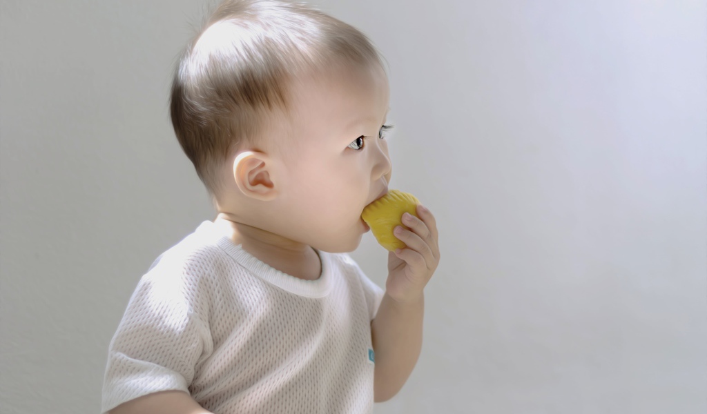 Маленький ребенок грызет игрушку на сером фоне