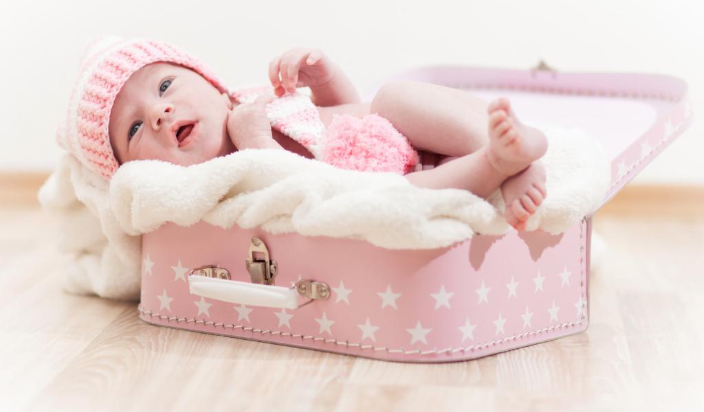 Маленький грудной ребенок спит в розовом чемодане