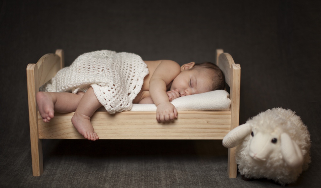 Маленький ребенок спит на деревянной кроватке с игрушкой