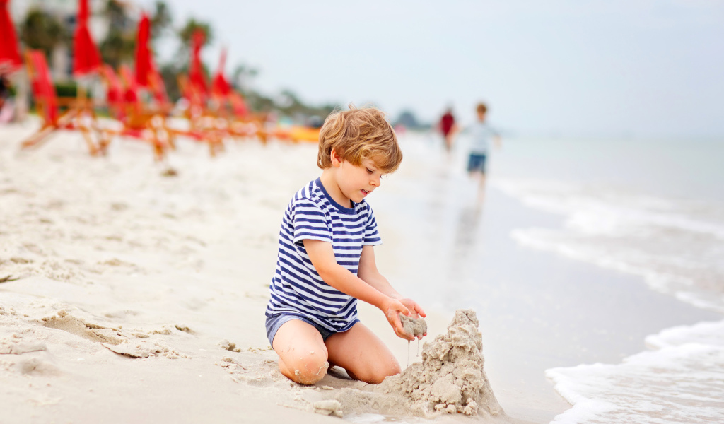 Маленький мальчик строит замок из песка на пляже