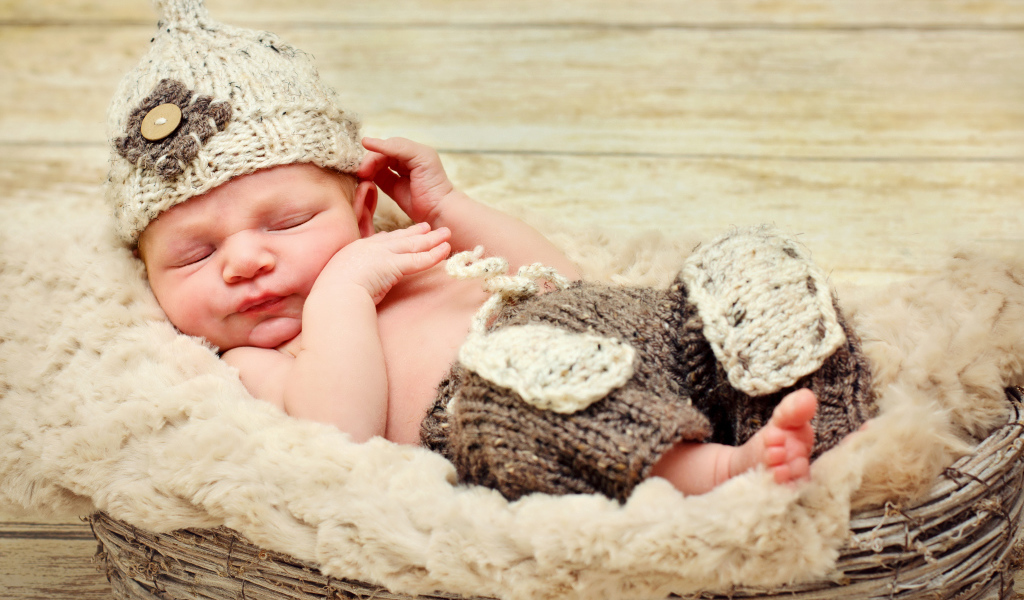 Маленький мальчик в вязаной шапке спит в корзине