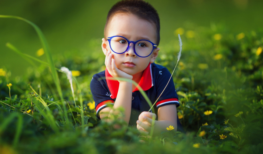 Маленький мальчик в очках лежит на зеленой траве