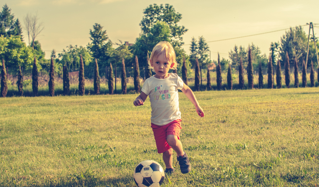 Маленький мальчик играет в футбол на зеленой траве