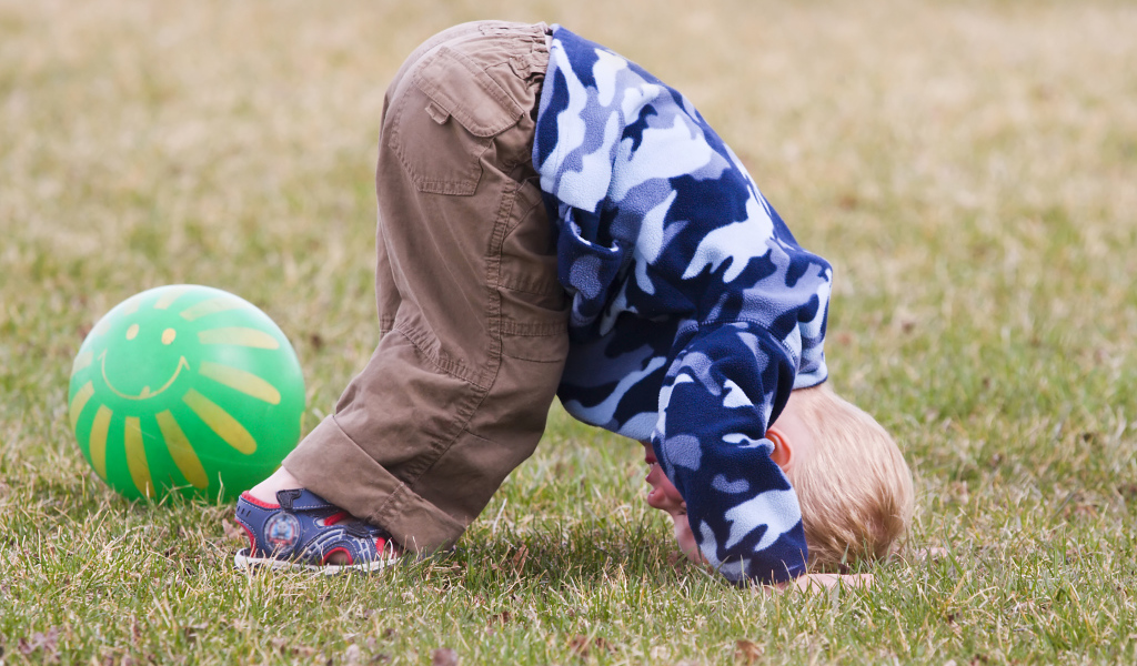 Маленький мальчик играет на траве с мячом