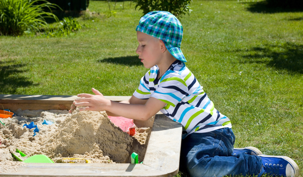 Маленький мальчик играет в песке на зеленой траве