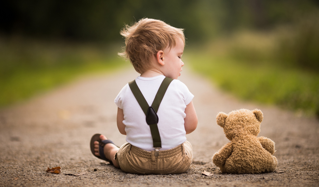 Маленький мальчик сидит на дороге с игрушечным мишкой