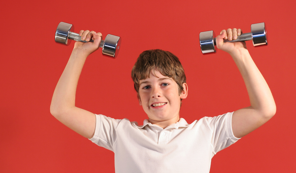Маленький мальчик с гантелями на красном фоне