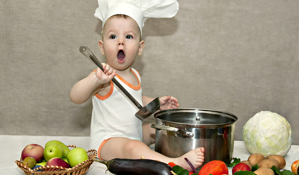 Маленький поваренок с кастрюлей на столе с овощами