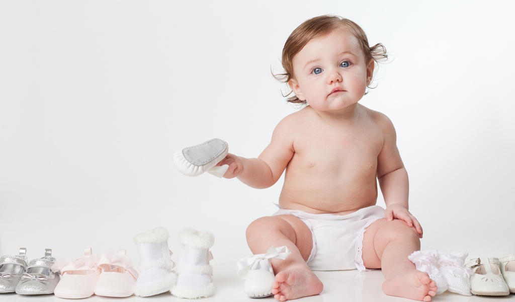 Маленький забавный голубоглазый малыш с обувью на белом фоне