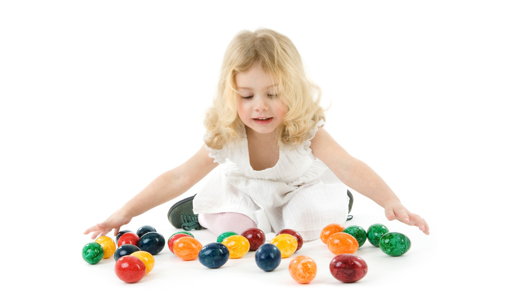 Маленькая девочка блондинка с крашеными яйцами на белом фоне