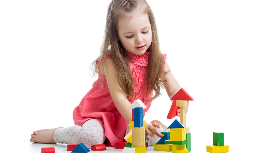 Маленькая девочка строит домик из кубиков на белом фоне