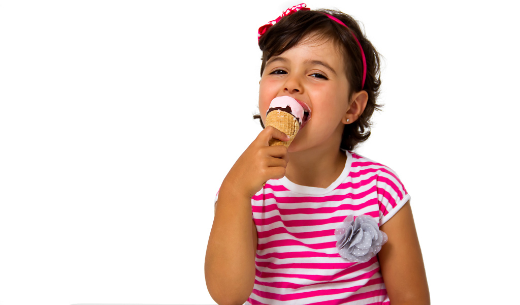 Маленькая девочка ест мороженое за столом на белом фоне